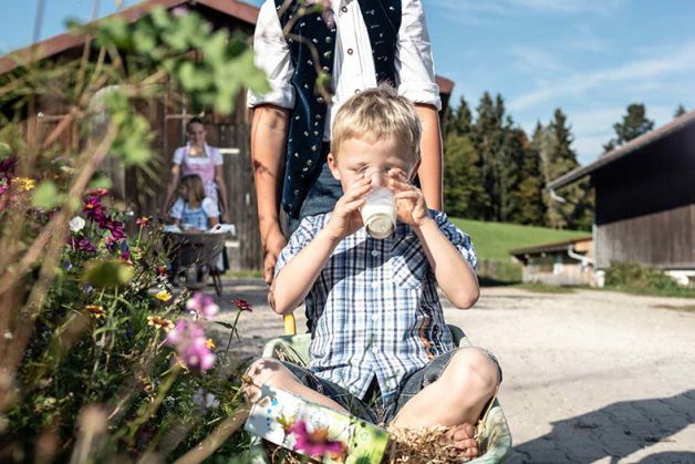 Junge sitzt in einer Schubkare und trinkt sternenfair Milch